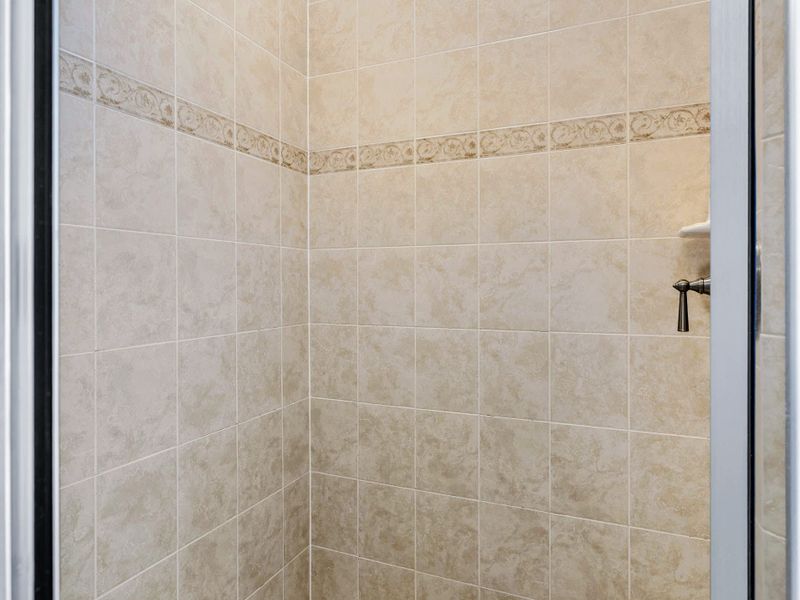 Primary Suite - Step inside the walk-in shower, warm neutral tile from floor to ceiling and an oversized showerhead.