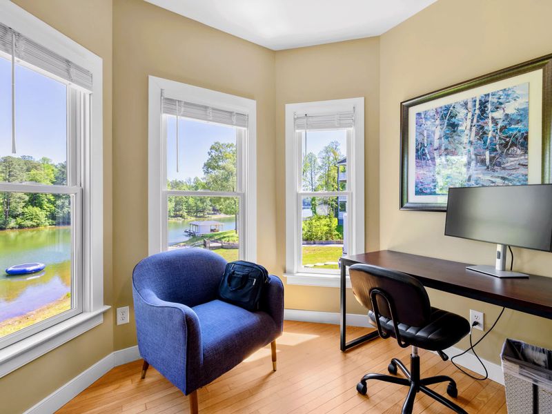 Primary Suite - A desk with monitor and a blue armchair share the corner nook, lake views filling all three windows.