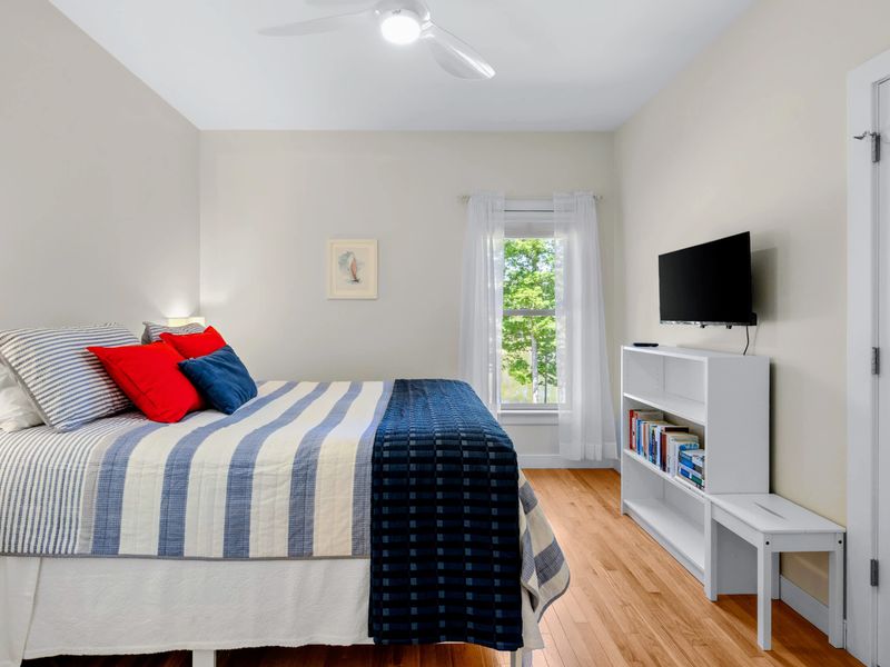 Queen Guest Bdrm - Queen bed in cheerful red, white, and blue, plus a TV and a shelf of books below.