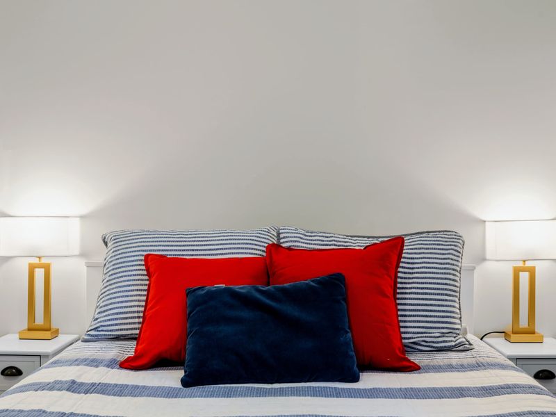 Queen Guest Bdrm - Crisp striped shams layered with red and navy pillows, twin lamps glowing on either side of the bed.