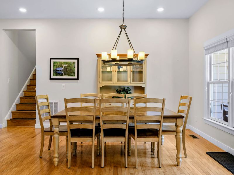 Dining Room - Eight ladder-back chairs around a long wood table, candle-style chandelier above and a glass-front hutch behind.