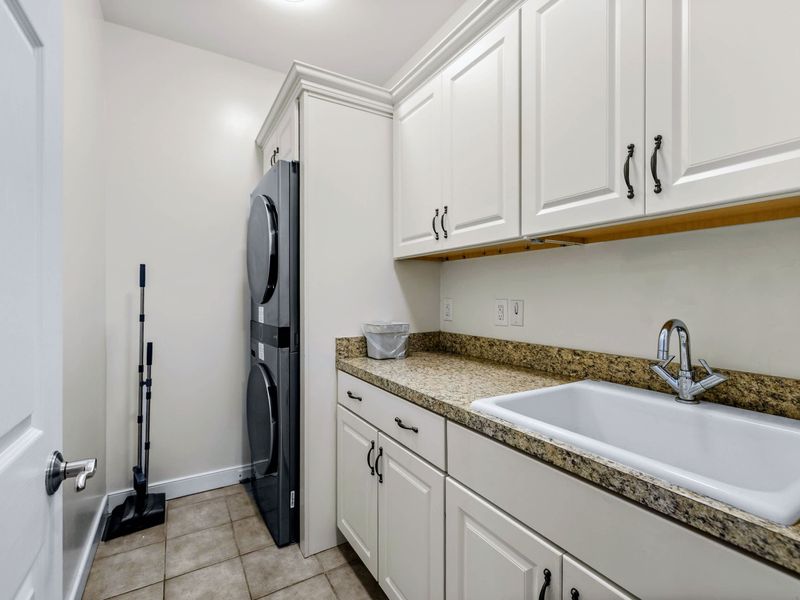 Upper Level Laundry - Stacked washer and dryer with a deep utility sink, granite counters, and cabinets for storage just off the kitchen.