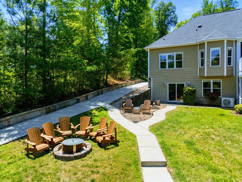 Lakefront - A winding path links the lower patio to the chair-ringed fire pit, woods wrapping the side yard in green.