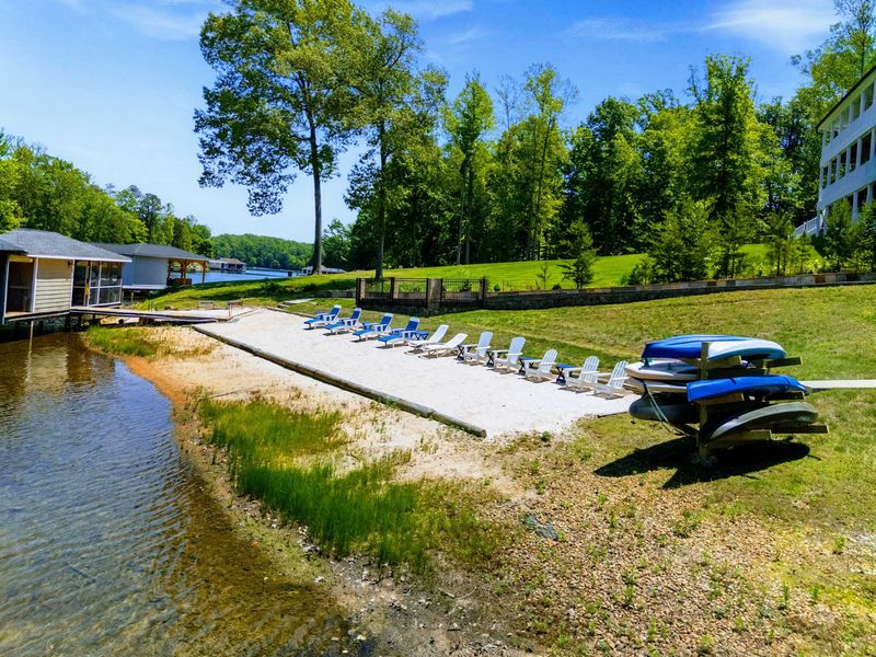 Lakefront - Stretching along the shore, the sandy beach holds a full lineup of chairs, with stacked kayaks and standup paddleboards waiting by the grass.