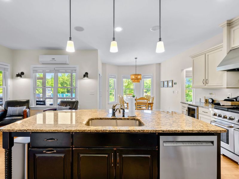 Kitchen - Straight-on look at the island sink and stainless dishwasher, pendants overhead and the dining bay glowing in the background.