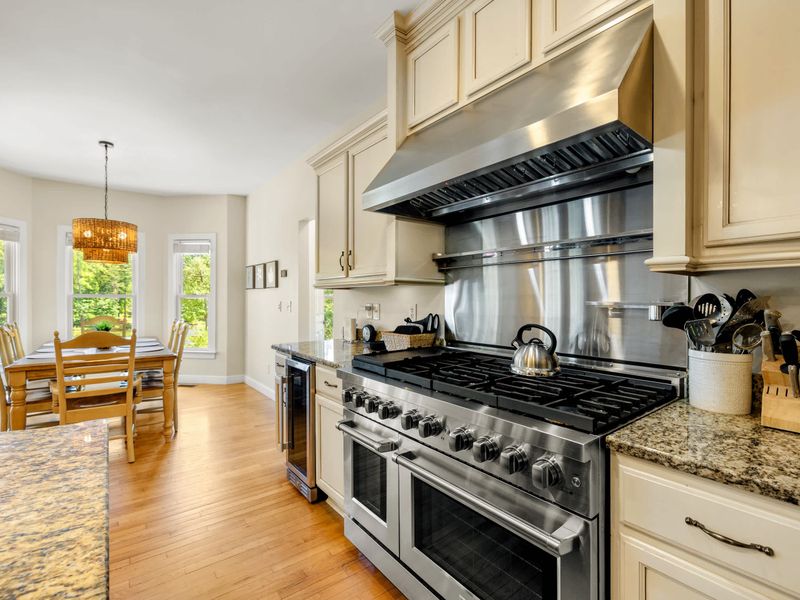 Kitchen - The stainless gas range anchors this wall, double ovens below a big vent hood, with the breakfast table catching morning light.
