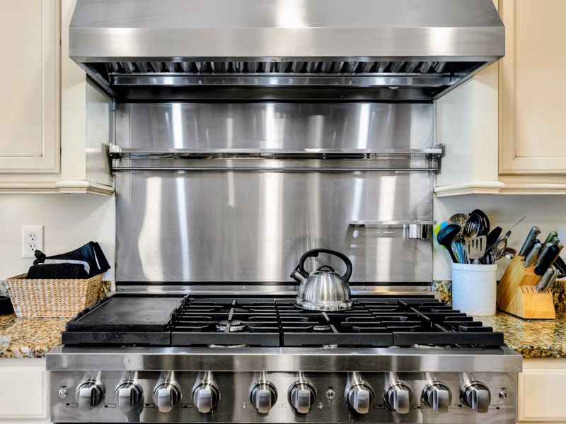 Kitchen - Up close with the pro-style gas range, tea kettle, stainless backsplash, and a knife block within easy reach.