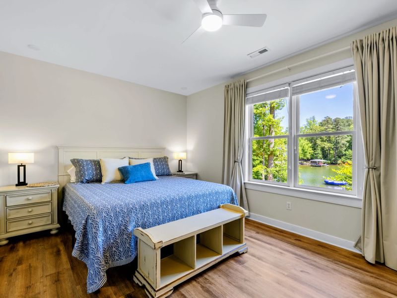 Lower King Guest Suite - King bed in crisp blue layers beside a big lake-view window, with twin lamps for nighttime reading.