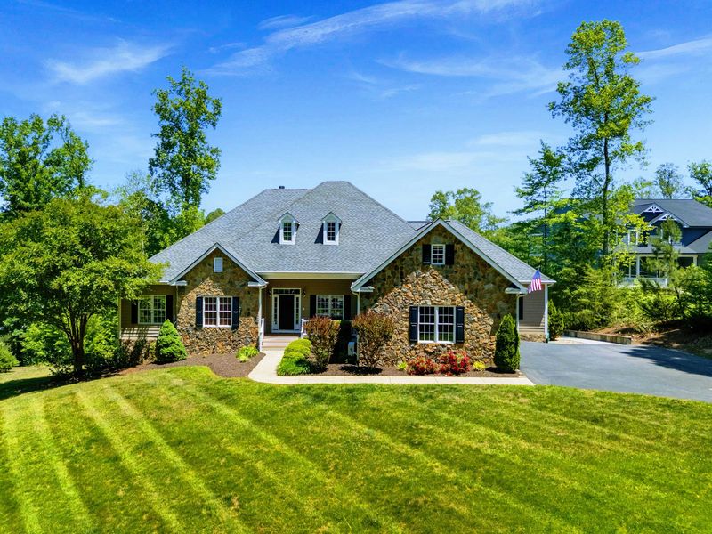 Exterior - Stone-accented facade and covered front porch, framed by mature trees and tidy landscaping and a paved private driveway.