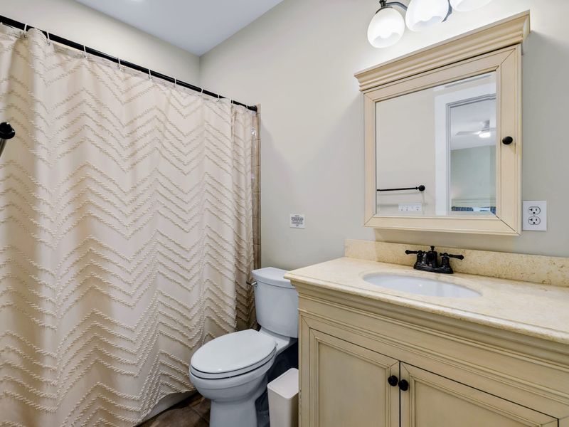 Lower King Guest Suite - Tidy bath with a cream vanity, lighted mirror cabinet, and a textured curtain across the shower.