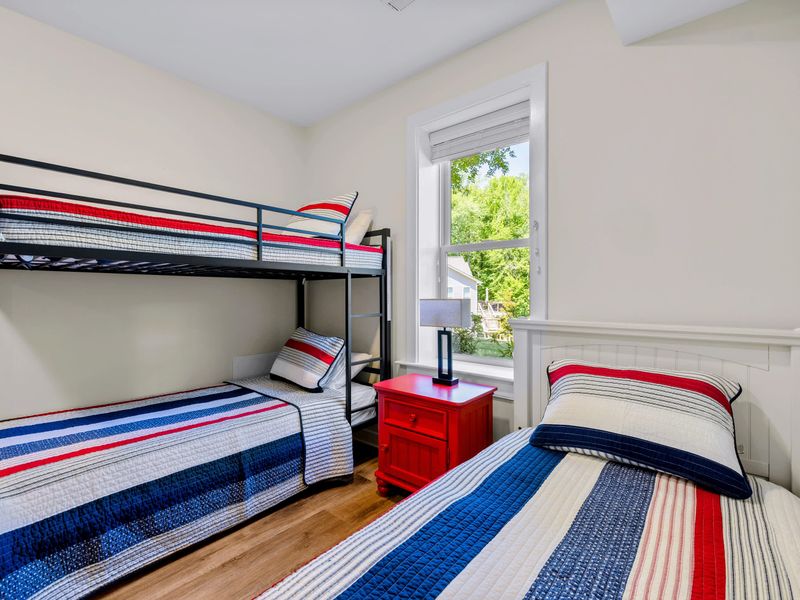 Lower Level Bunk Suite - Sunlight lands on the metal bunk's striped quilts, with another twin bed and lamp close by.