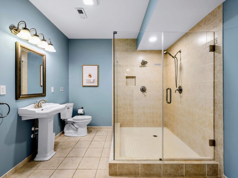 Lower Level Bathroom - Spacious glass walk-in shower with a handheld sprayer, plus a classic white pedestal sink against soft blue walls.