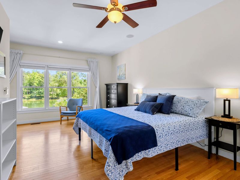 Secondary Suite - A blue-dressed king bed under a ceiling fan, with big windows pulling in the water through the trees.