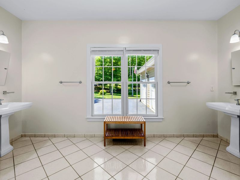 Secondary Suite - Twin pedestal sinks face each other across the tiled ensuite, a wooden bench resting under the bright window.