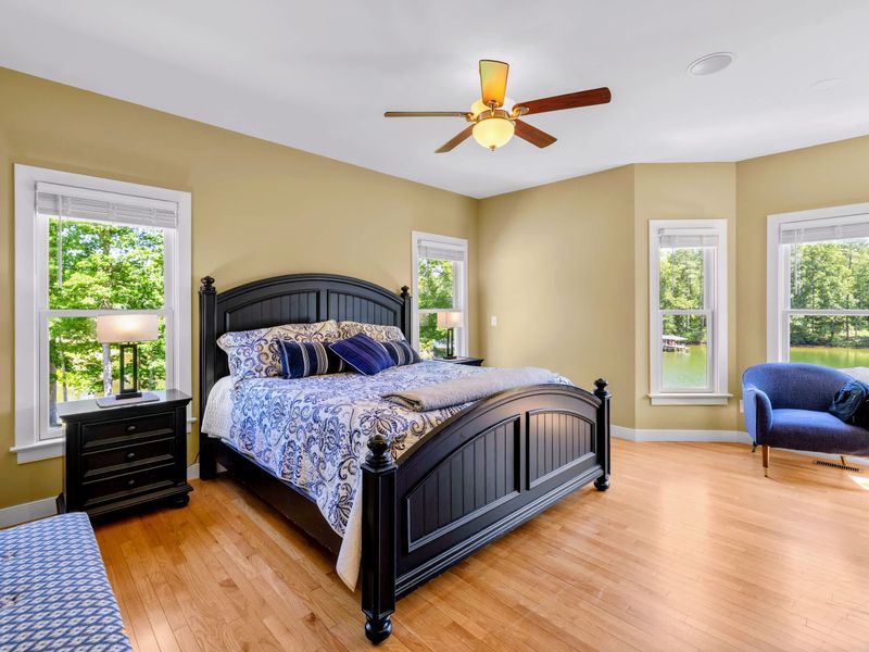 Primary Suite - King bed in soothing blues, corner windows framing a gorgeous sunrise view of the water, and a navy armchair for slow mornings.