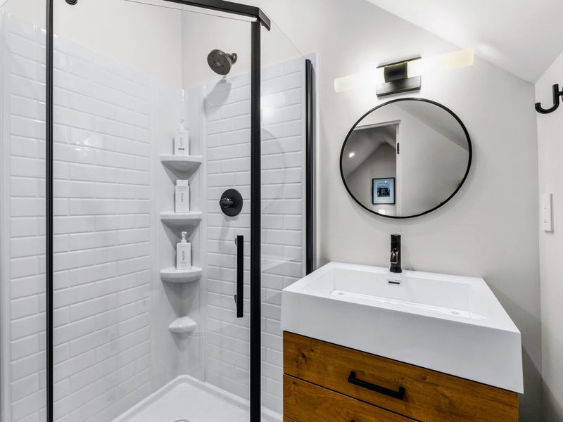 Library Suite - The ensuite glass shower with a round mirror and wood vanity.