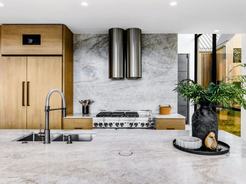 Chef's Kitchen - Quartzite backsplash, pro gas range, and warm wood cabinetry, open to the living space.