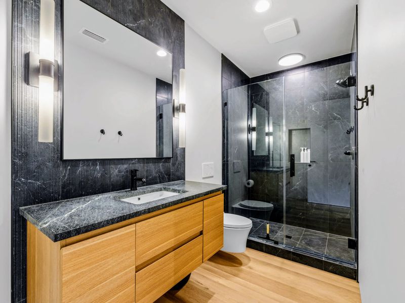 King Bedroom 6 - A dark-tile ensuite with a glass shower and warm wood vanity.