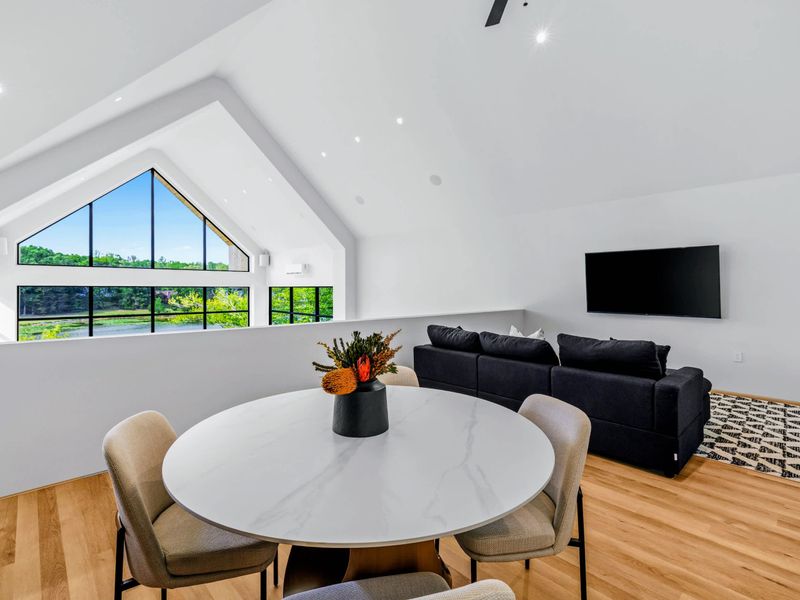 Loft Lounge - A round table and sofa tucked beneath the A-frame glass, treetops outside.
