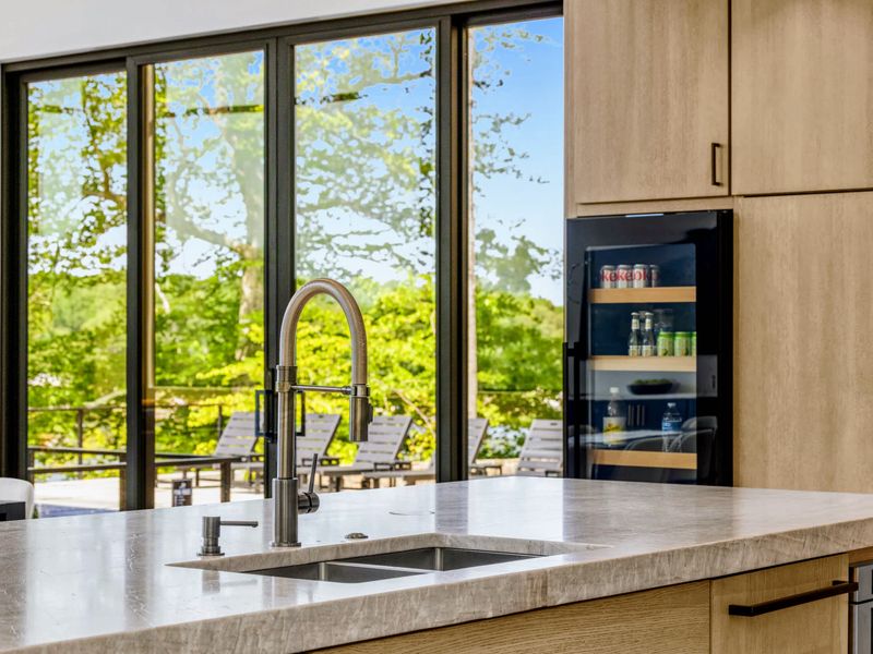 Chef's Kitchen - A black stainless steel faucet at the sink with forest views and a wine fridge close at hand.