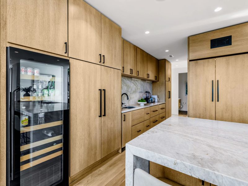 Kitchen - Wine storage and clean wood cabinetry frame the quartzite island.