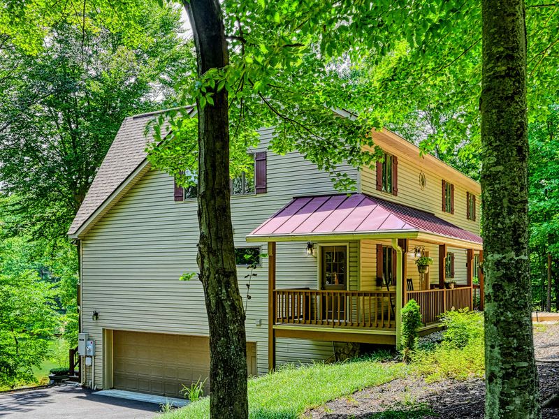 Wooded Setting - The home tucked into mature trees, its covered porch and garage framed by greenery.