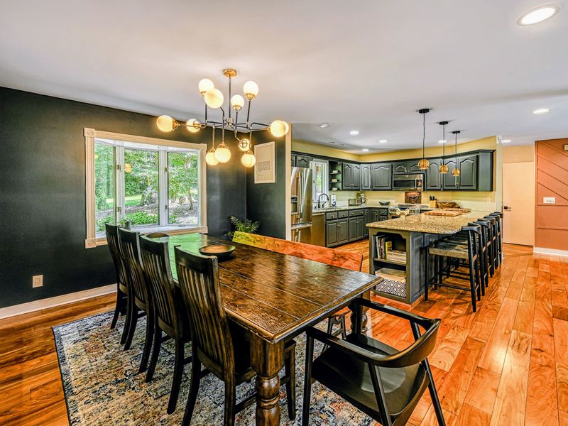 Dining Area - A long farmhouse table under a modern chandelier, set against a deep green accent wall.