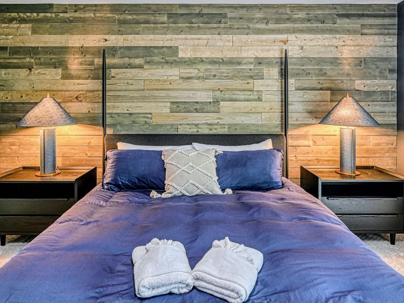 Primary Suite - The king bed rests against a warm reclaimed-wood accent wall, framed by wicker-shade lamps.