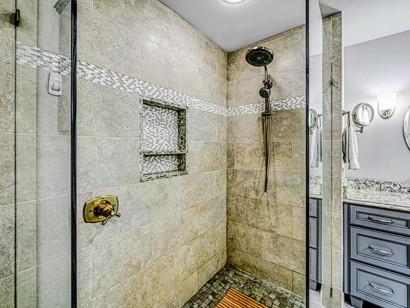 Spa Shower - Stone tile with a mosaic-trimmed niche and a rainfall-and-handheld shower head.