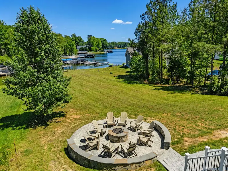 Lakeside Fire Pit - Adirondack chairs ring the built-in gas fire pit, with the dock, boathouse, and open water filling the view beyond.