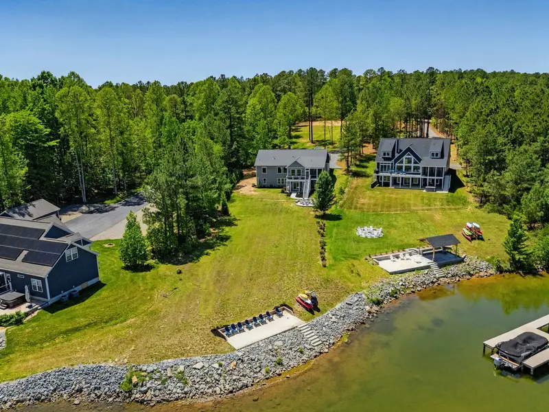 Aerial Setting - The property's wide lawn rolls from the home down to a private fire pit, kayak rack, and dock on the calm cove.