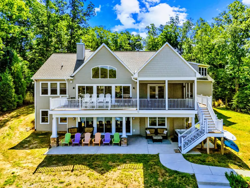 Rear Exterior - The lake-facing side opens across two deck levels, a screened porch, and a patio lined with bright Adirondack chairs.