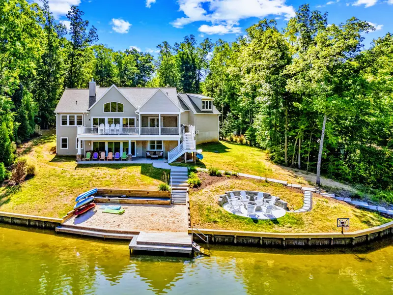 Aerial View - The whole retreat from above: tiered lawn down to a sandy beach, fire pit circle, private dock, and two-story boathouse on the water.