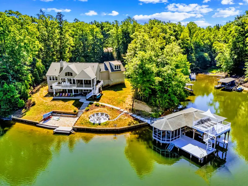 Aerial View - The full lakefront setup at a glance: open lawn, fire pit, sandy beach, dock, and boathouse steps from the back door.
