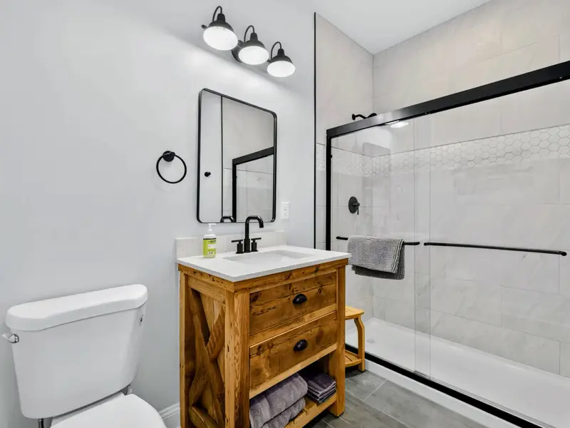 Lower Bathroom - A reclaimed-wood vanity with quartz counter and black fixtures pairs with a glass-enclosed shower wrapped in soft marble-look tile.