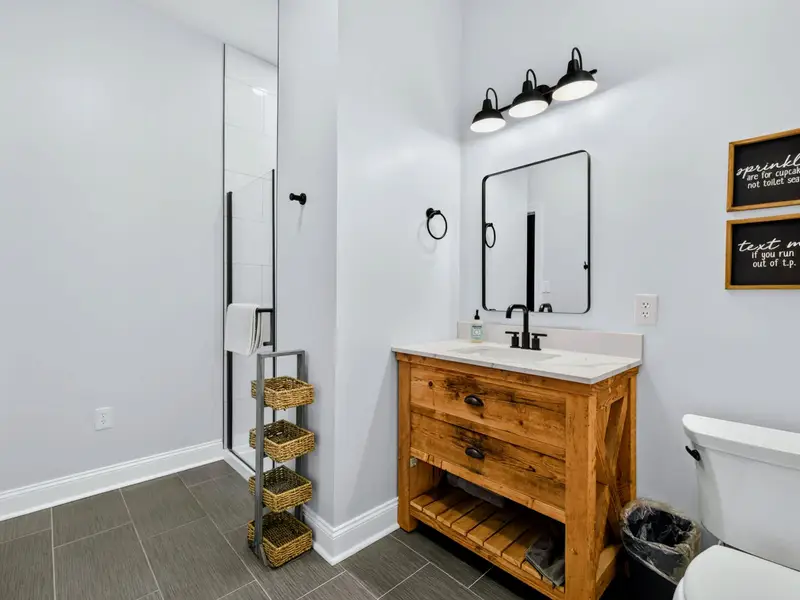 Bunk Bathroom - A reclaimed-wood vanity and quartz counter, black fixtures, and a basket ladder stacked with towels bring warm farmhouse character to this full bath.