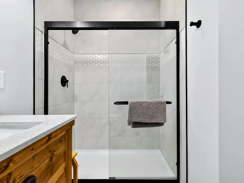 Lower Bathroom - The walk-in glass shower is finished in marble-look tile with a hexagon accent band and matte black fixtures, clean and spa-like.