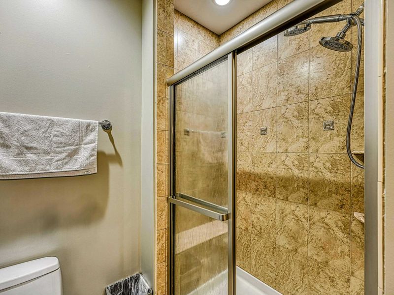 Lake Level Bath - A glass-enclosed walk-in shower with stone tile and a handheld showerhead.