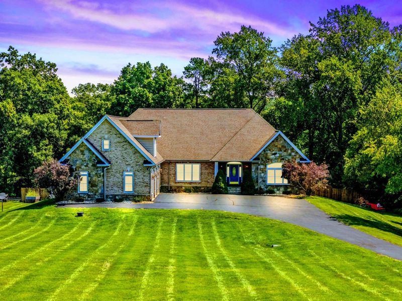 Exterior - The stone-and-stucco home at twilight, with a manicured lawn, circular drive, and landscape lighting.