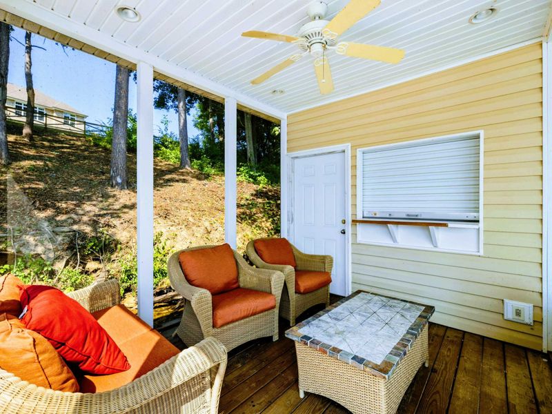 Boathouse - The screened-in lounge inside the boathouse, with wicker seating, a ceiling fan, and the hillside rising behind.
