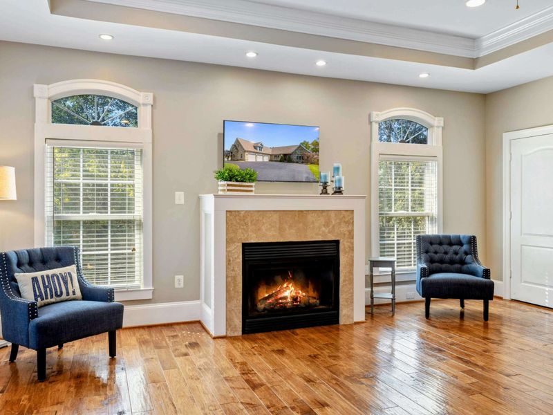Primary Suite - The fireplace sitting area with a Smart TV, flanked by arched windows and two navy accent chairs.