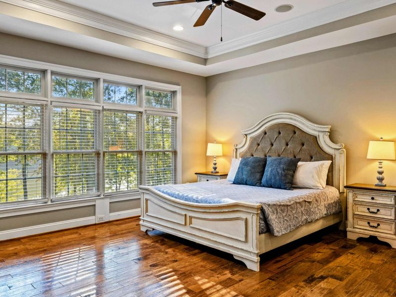 Ensuite 2 - A king bed with tufted headboard, tray ceiling, and large windows looking out to the trees.