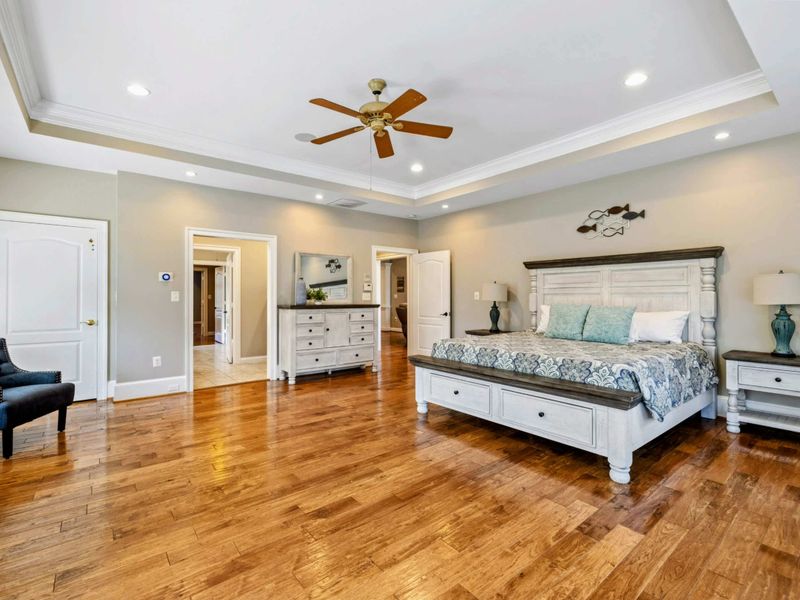 Primary Suite - From the bed, doorways lead to the walk-in closet and ensuite bath, with a dresser and seating chair.