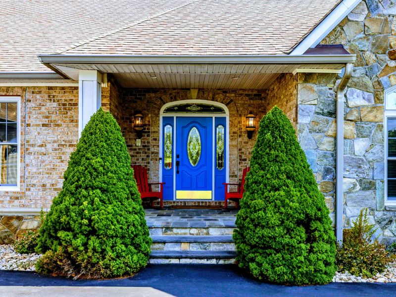 Front Entry - A blue stained-glass door flanked by manicured evergreens and stone steps welcomes you in.