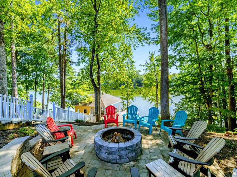 Fire Pit - Colorful Adirondack chairs circle the stone fire pit, with the lake shimmering through the trees.
