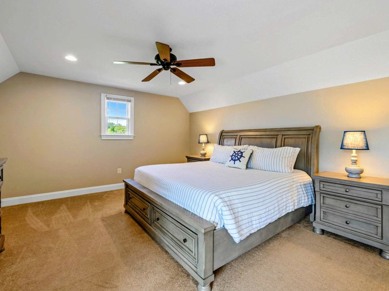 Upper Suite - A king bed with nautical bedding, vaulted ceiling, and a window seat overlooking the grounds.