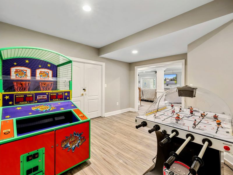Game Room - A basketball arcade and rod hockey table in the bonus room, with the movie theater visible through the doorway.
