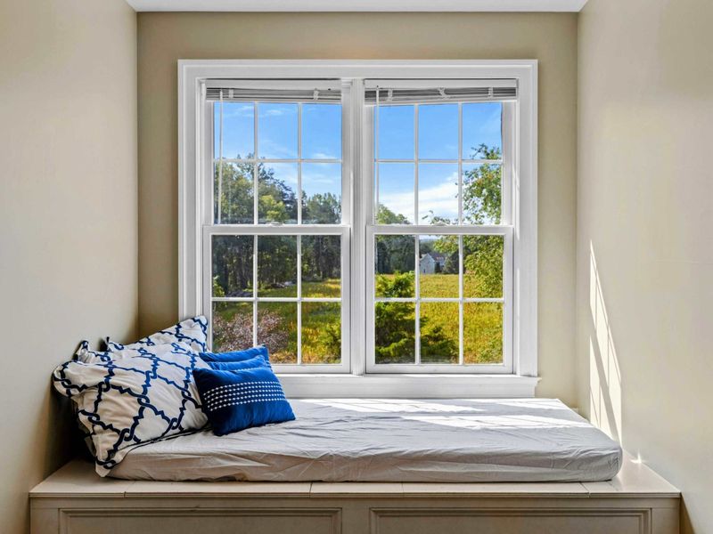 Upper Suite - A cozy window seat with pillows and a view of the property's green surroundings.