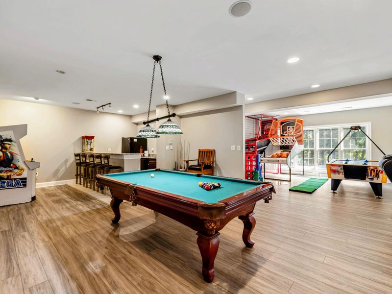 Game Room - The full game room: pool table under pendant lights, vintage Sega arcade, basketball machines, and a bar area beyond.