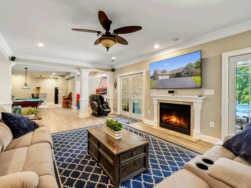 Living Area - A large sectional, electric fireplace, and wall-mounted TV open to the game room beyond, with a massage chair by the door.